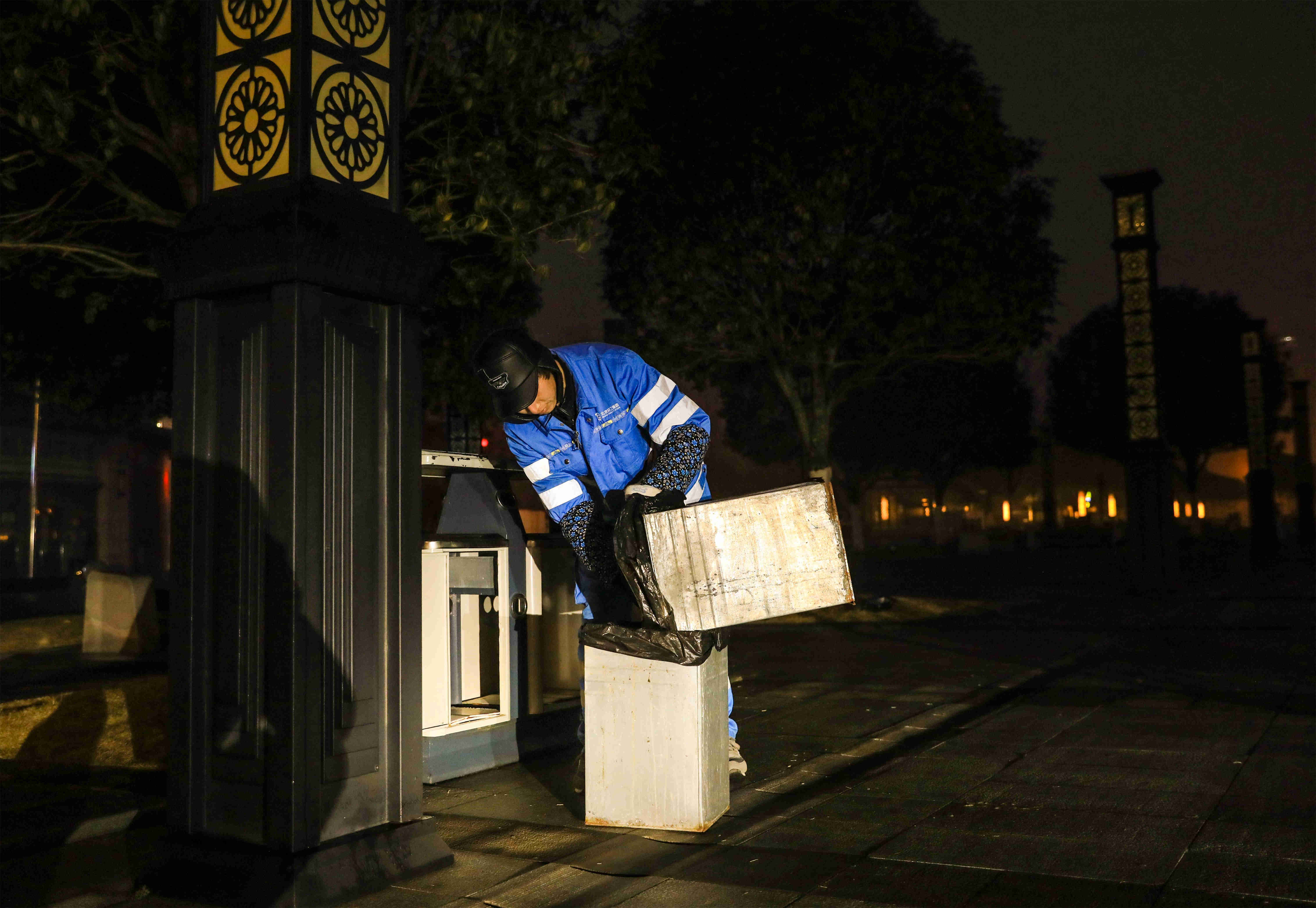 清晨,清洁工张兴中在都梁广场清理垃圾桶内的垃圾(摄影:熊伟)